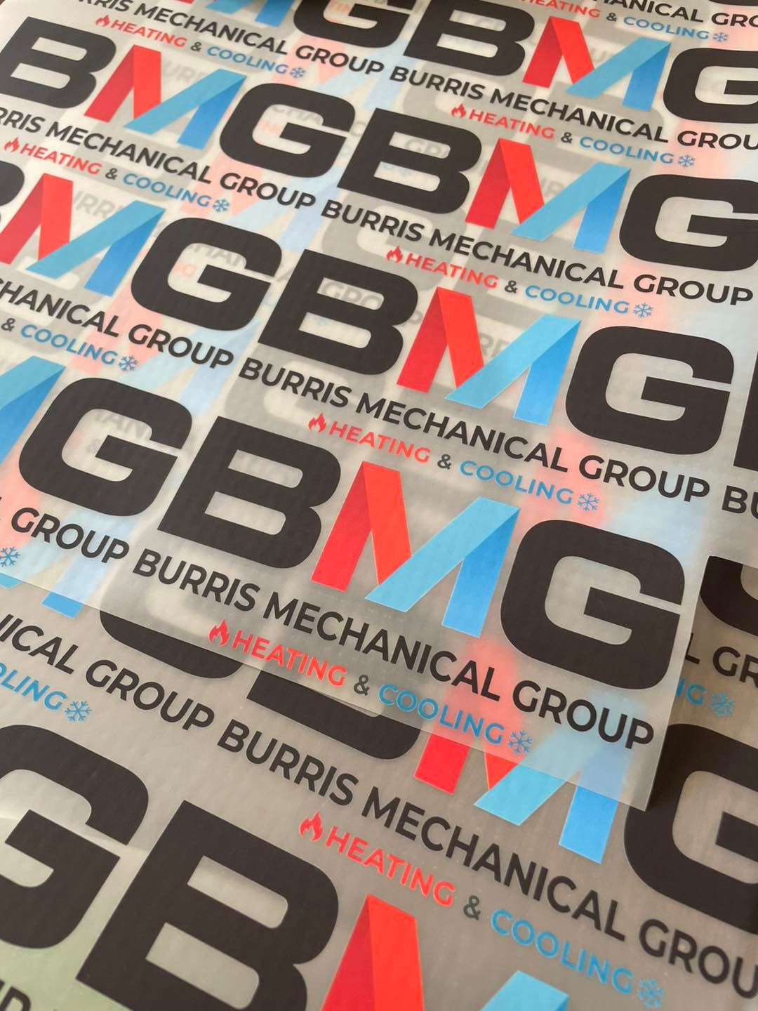 Stacked DTF transfer sheets printed with the Burris Mechanical Group heating and cooling logo